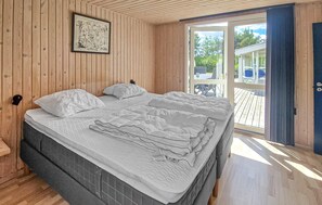 A wooden-paneled bedroom with a large bed, a small table, and a door leading to an outdoor area. - 3 bedroom gorgeous home in Hadsund (Hadsund)