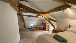A bedroom with a sloped ceiling, wooden beams, a bed with white linens, and a window with curtains.