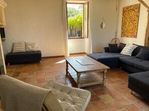 A living room with a sofa, a coffee table, and a chair. There is a window with curtains, a painting on the wall, and a tiled floor. - Beautiful Farmhouse in South of France (Bourlens)