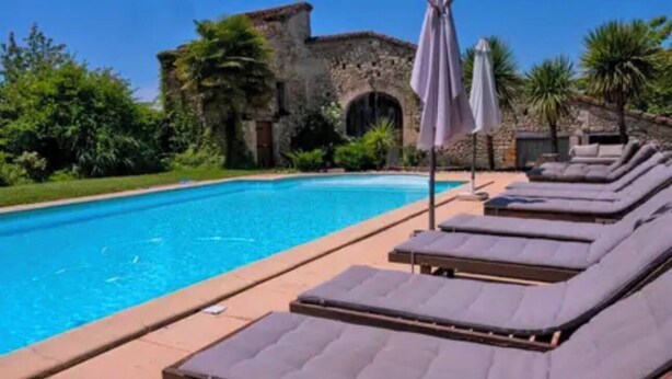 A swimming pool with lounge chairs and a stone building in the background.