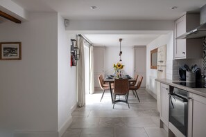 A modern kitchen with a dining area, featuring a central island, pendant lighting, and a view into the dining room. - Bayholme House - Luxury Cottages (Oxwich)