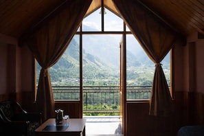 Ein Zimmer mit einem großen Fenster, Vorhängen, einem Tisch mit Teekanne und einem Sessel.