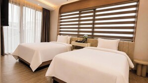 A hotel room with two beds, a wooden headboard, a bedside table with a phone, and a window with blinds. - DOM HOTEL DALAT (Lam Vien - Da Lat)