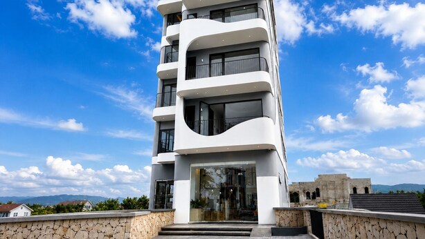 A modern multi-story building with a curved facade, large windows, and a stone base. - DOM HOTEL DALAT (Lam Vien - Da Lat)