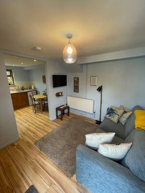 A living room with a grey sofa, a wooden dining table, and a kitchen in the background. - Apartment Sleeps 3 With Parking (Swansea)