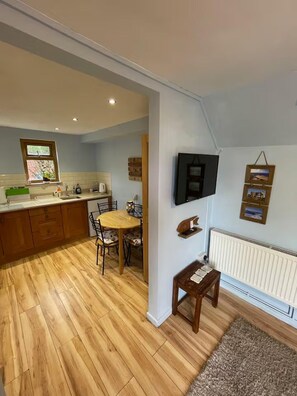 A compact kitchen with a dining area, a flat-screen TV mounted on the wall, and a small table with a rug. - Apartment Sleeps 3 With Parking (Swansea)