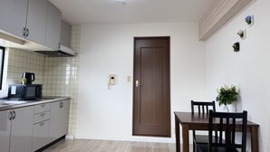 A compact kitchen with a microwave, a coffee maker, and a cabinet. There is a wooden door and a dining table with chairs. - Raku Osaka Daikokucho Namba Shinsaibashi (Osaka)
