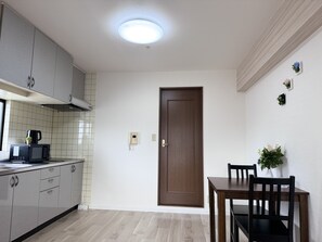 A compact kitchen with a microwave, a coffee maker, and a cabinet. There is a wooden door and a dining table with chairs. - Raku Osaka Daikokucho Namba Shinsaibashi (Osaka)