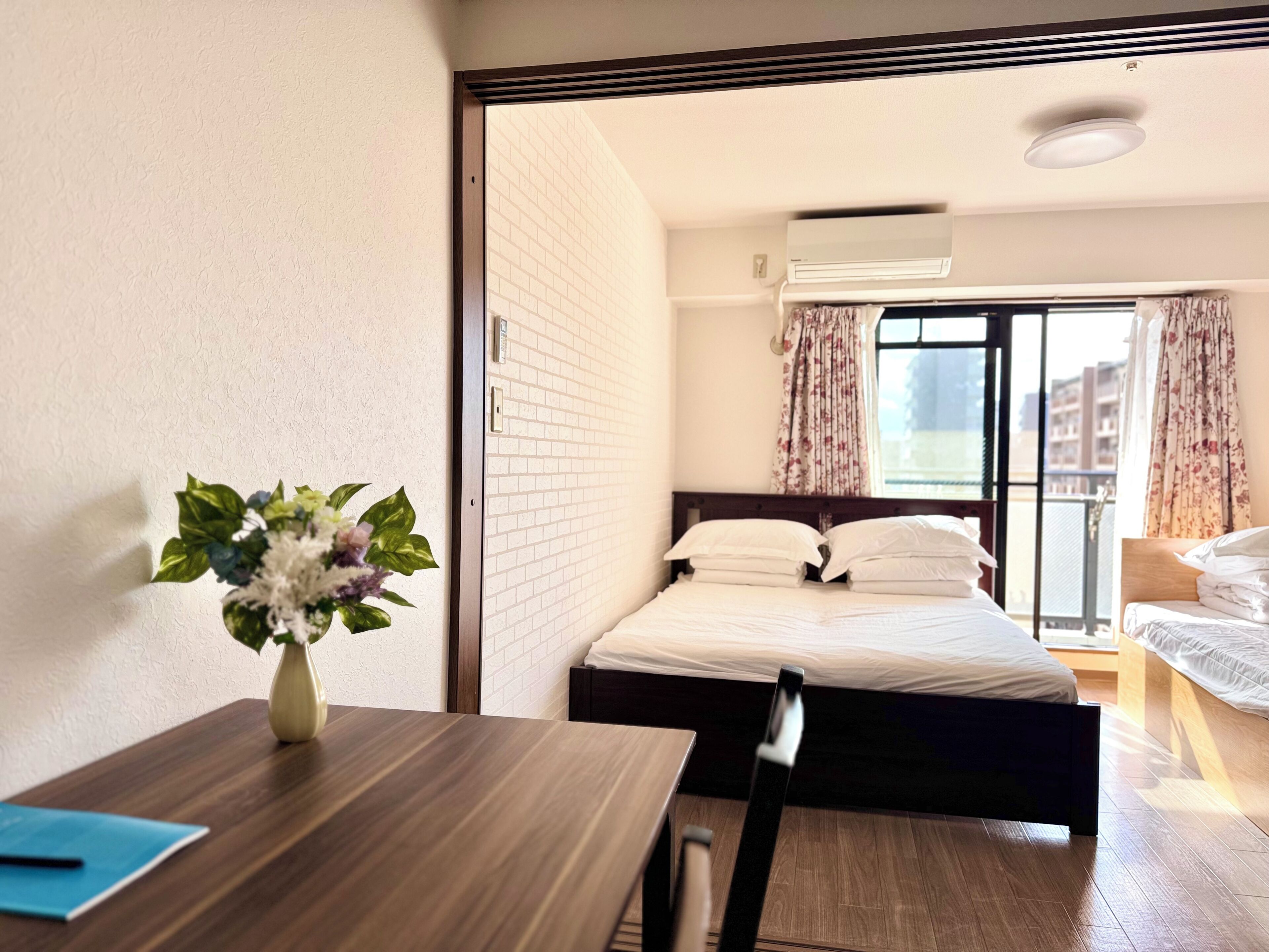 Habitación de hotel con una cama, un escritorio y un florero, y vista al exterior.