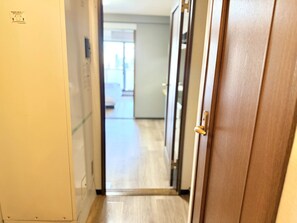 A hallway leading to a room with a wooden door and a visible light switch on the wall. - Raku Osaka Daikokucho Namba Shinsaibashi (Osaka)