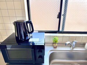 A kitchen with a microwave and a black coffee maker on the counter. - Raku Osaka Daikokucho Namba Shinsaibashi (Osaka)