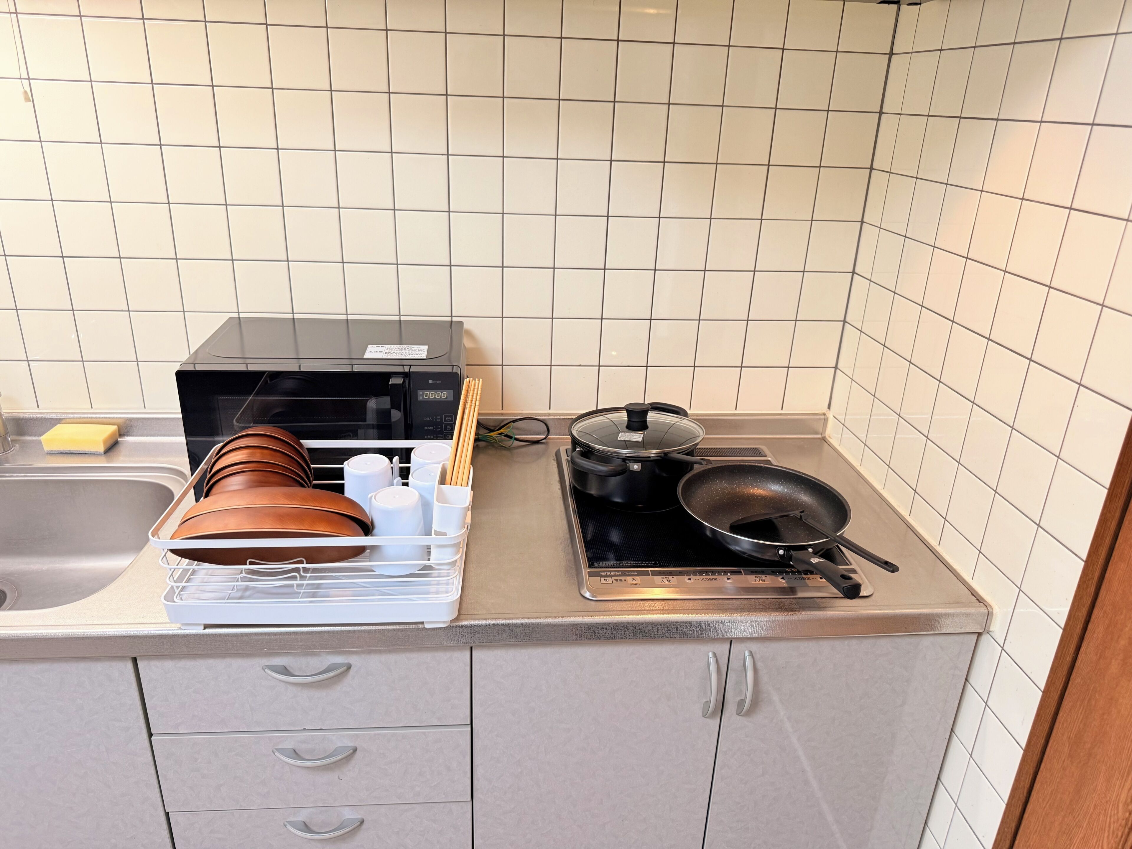 A kitchen with a microwave, a frying pan, a pot, and a dish rack with utensils.