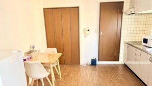 A kitchen with wooden flooring, a dining table with chairs, a refrigerator, and a microwave. - Raku Osaka Daikokucho Namba Shinsaibashi (Osaka)