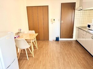 A kitchen with wooden flooring, a dining table with chairs, a refrigerator, and a microwave. - Raku Osaka Daikokucho Namba Shinsaibashi (Osaka)