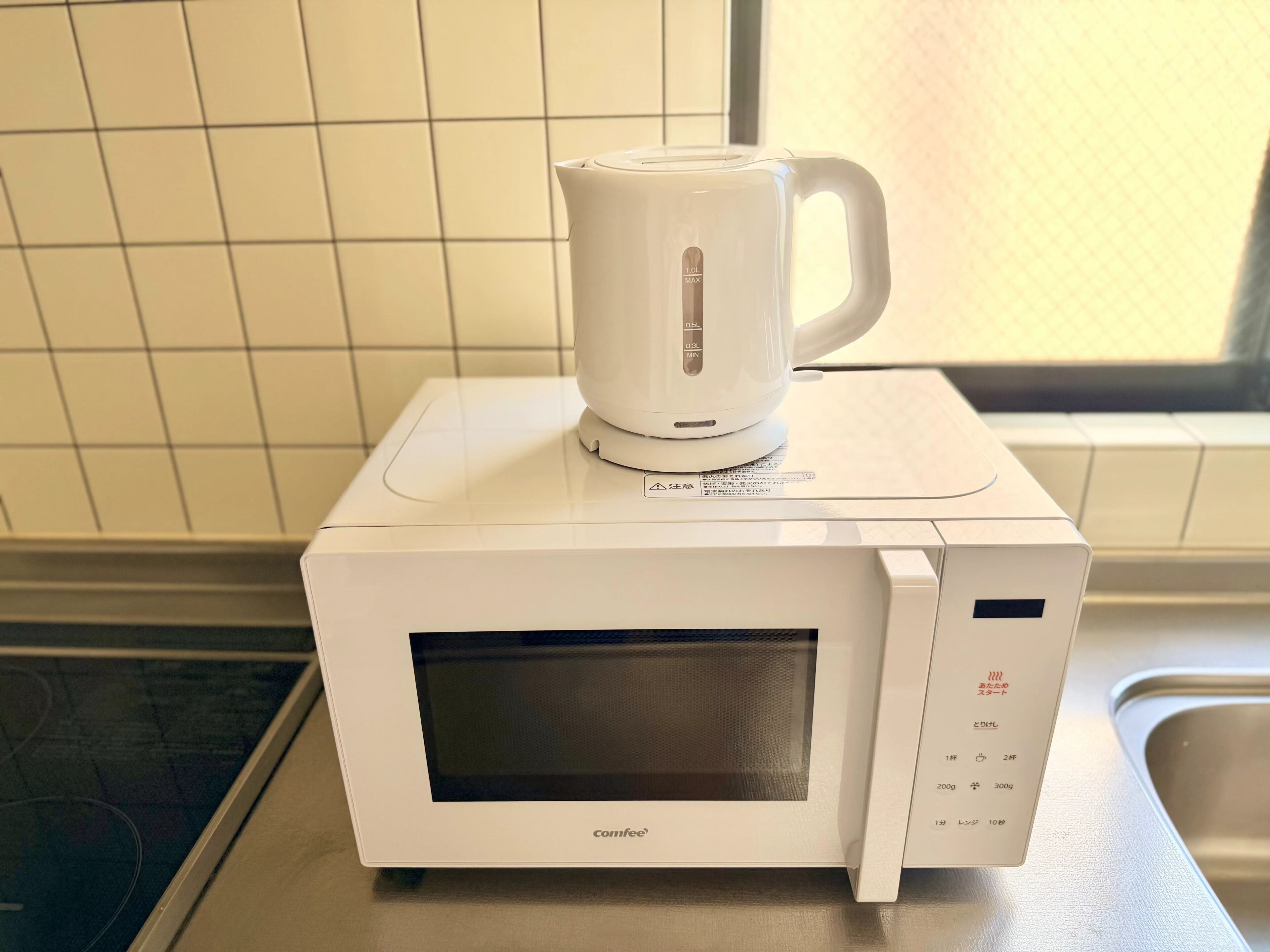 A compact microwave oven with a digital display and a kettle on top.