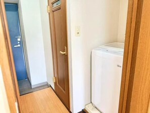 Ein schmaler Flur mit einer Holztür und einem weißen Gerät, vermutlich einem Kühlschrank, auf der rechten Seite.