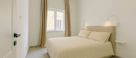 A bedroom with a bed, curtains, a window, and a wall-mounted light fixture.