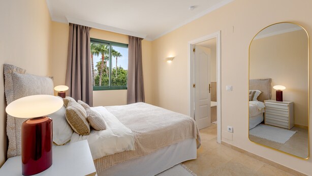 Un dormitorio con cama, lámparas de noche, un espejo grande y una ventana con cortinas.