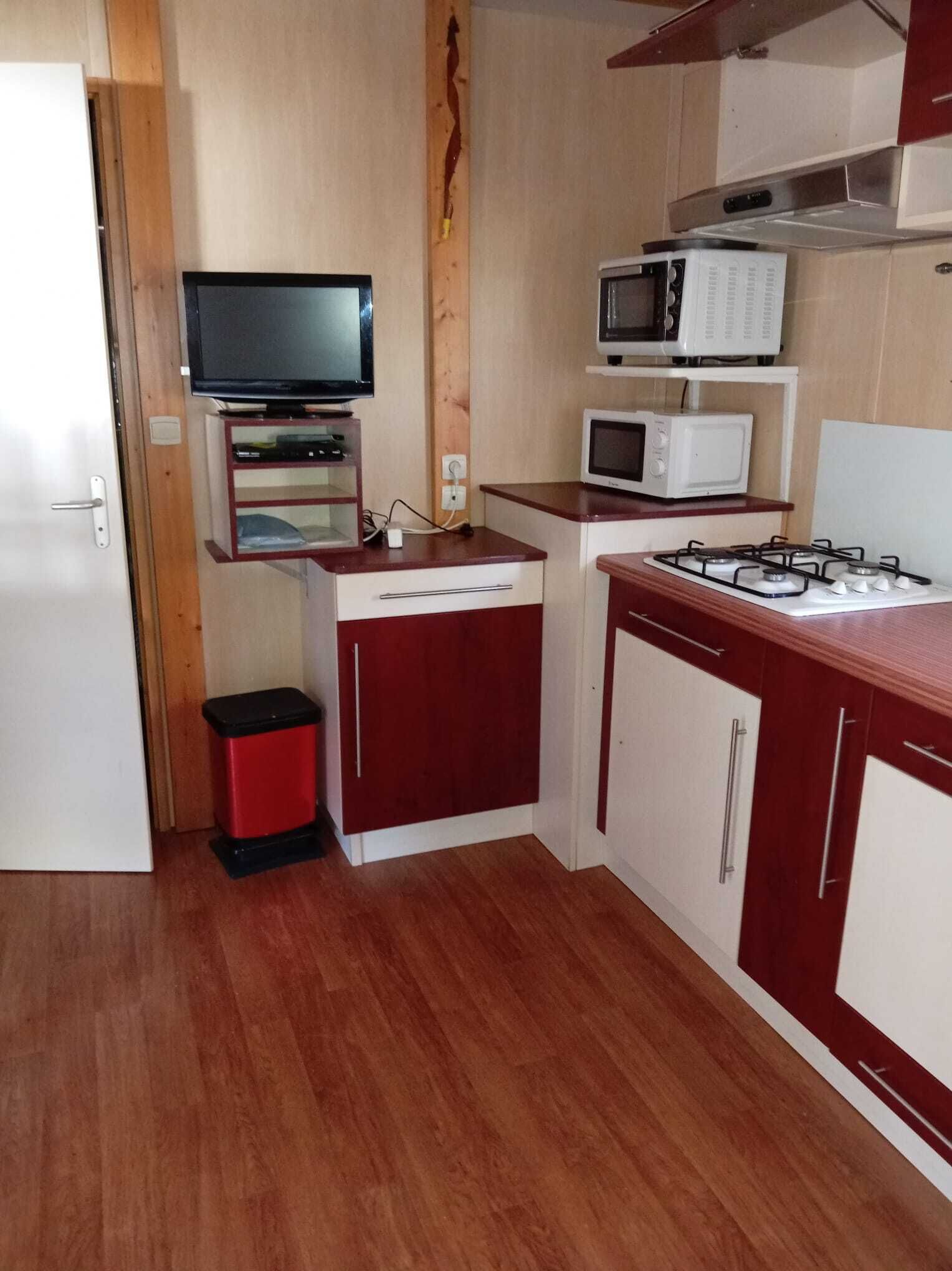 A compact kitchen with a microwave, stove, and a television on a shelf.