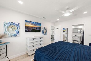 Een slaapkamer met een bed, een dressoir, een plafondventilator en kunstwerken aan de muur.