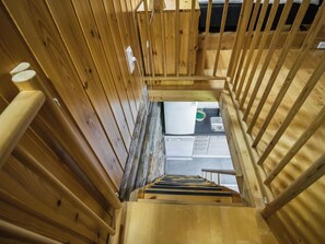 Eine Holztreppe führt zu einem Raum mit einem Bett, einem Nachttisch und einem Fenster.
