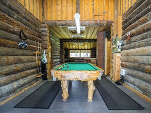 Ein gemütliches Holzblockhaus-Interieur mit Billardtisch, Feuerlöscher und einer Tür zu einem weiteren Raum.