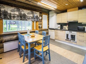 Ein Holzblockhaus-Interieur mit Essbereich, Küche und großen Fenstern mit Blick auf einen Wald.