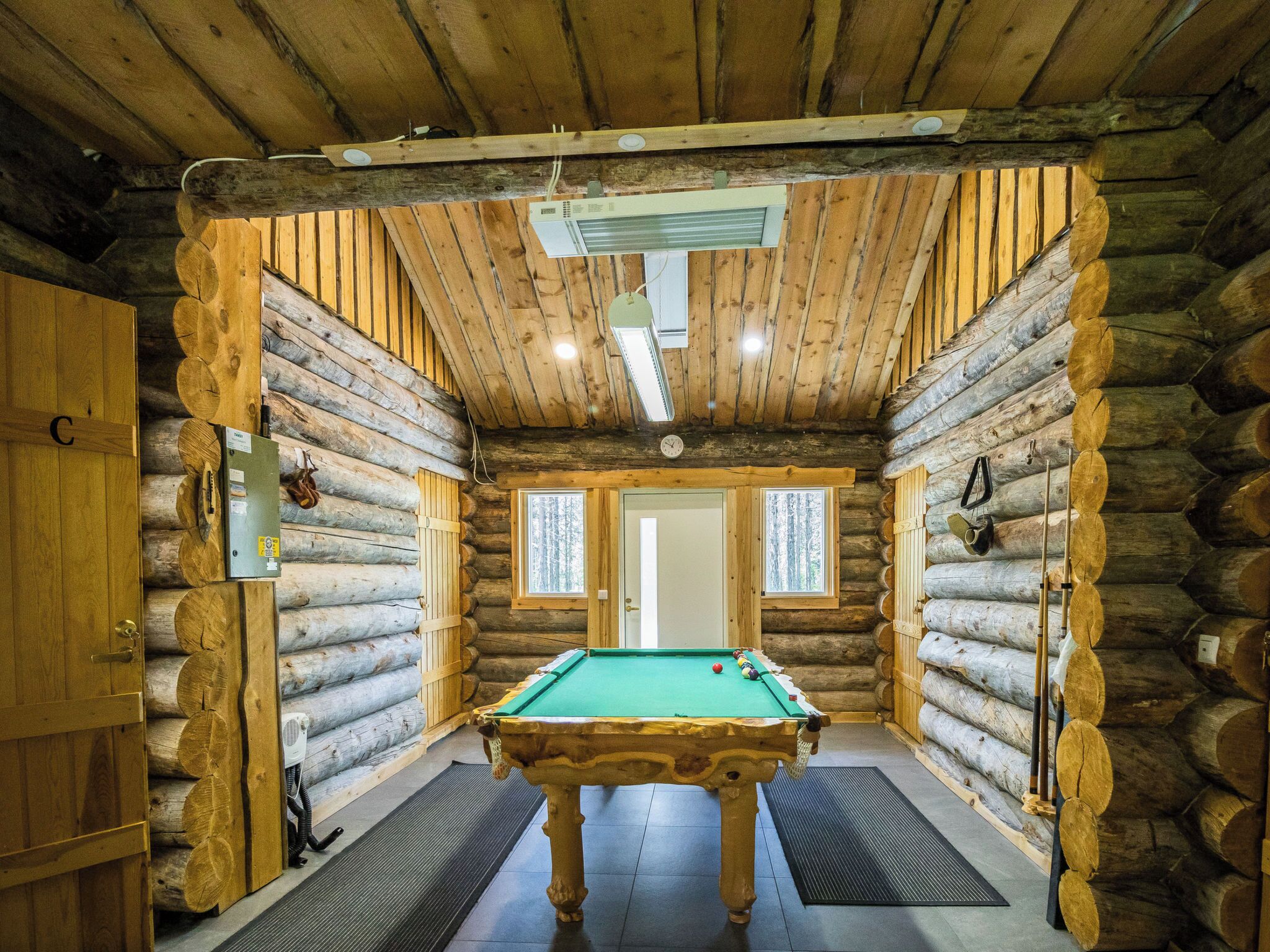 A log cabin interior with a pool table, wooden walls, and a ceiling fan.