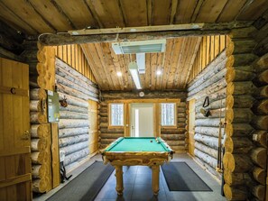 Ein rustikales Blockhaus-Interieur mit Billardtisch, Holzwänden und Deckenventilator.