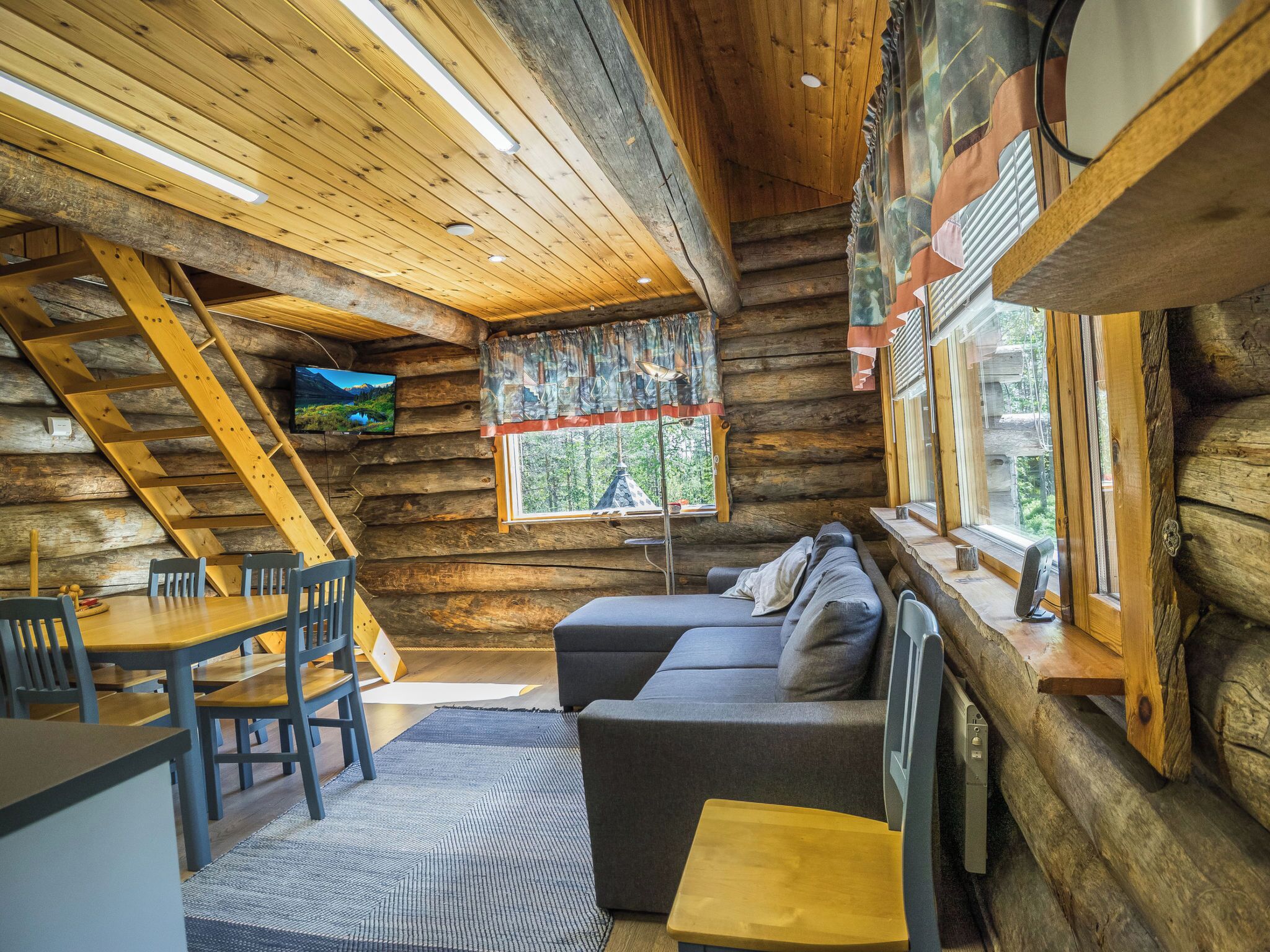Ein Blockhaus-Interieur mit Essbereich, Sofa und einem an der Wand montierten Fernseher.