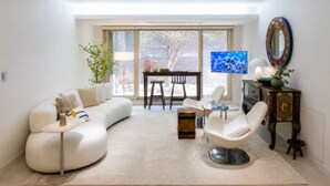 Una sala de estar moderna con un sofá curvo, un sillón blanco, una mesita redonda y un televisor.