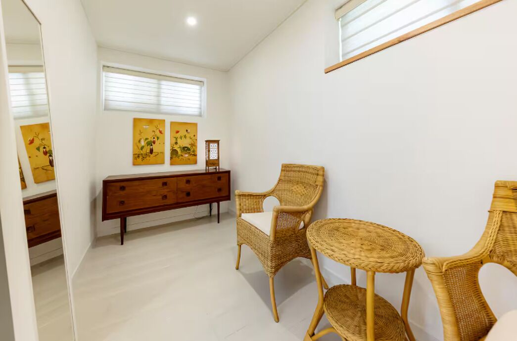 Una habitación con un aparador de madera, dos sillas de mimbre, una mesita redonda y una obra de arte en la pared.