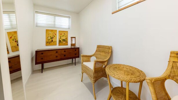 Una habitación con un aparador de madera, dos sillas de mimbre, una mesita redonda y una obra de arte en la pared.