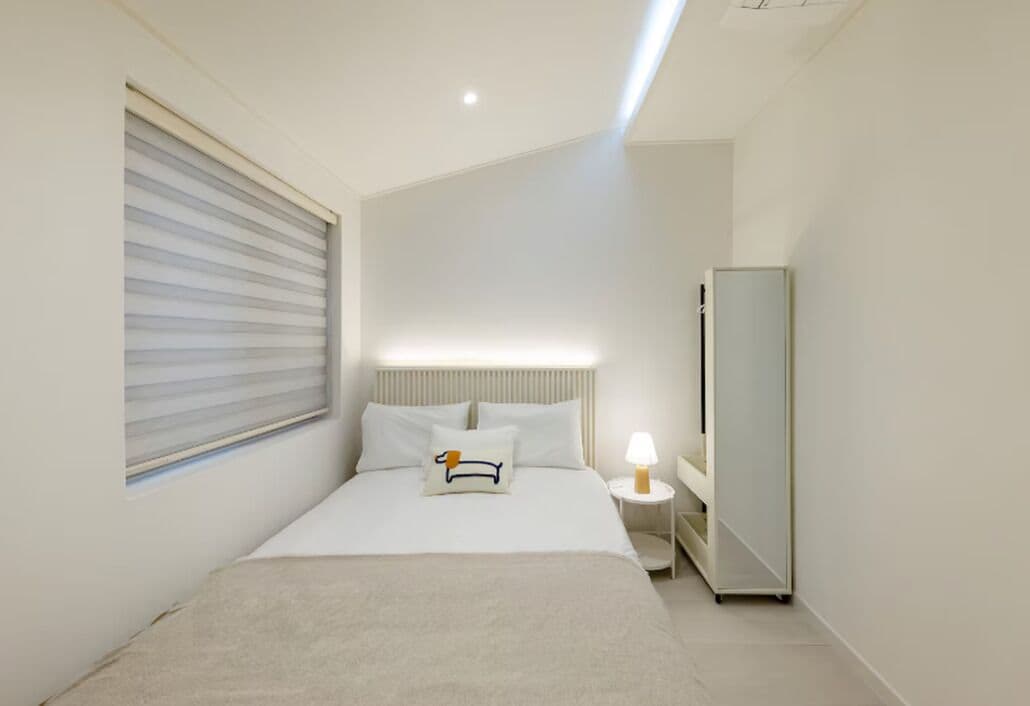 Quarto de hotel moderno com cama, mesa de cabeceira, abajur e um espelho grande.