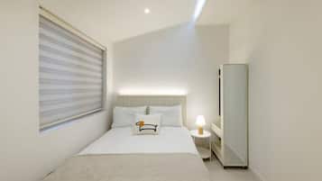 Quarto de hotel moderno com cama, mesa de cabeceira, abajur e um espelho grande.