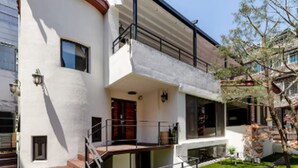 Una casa de dos pisos con un balcón, un pequeño jardín delantero y una escalera que lleva a la entrada.