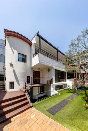 Una casa a due piani con un balcone, un piccolo giardino antistante e una scalinata che conduce all'ingresso.