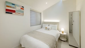 Habitación de hotel con cama, mesita de noche con lámpara, espejo y un cuadro en la pared.