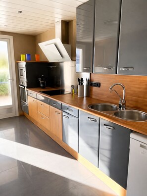 A modern kitchen with stainless steel appliances, wooden cabinets, and a double sink. - PARK de MAR Apartment (Sitges)
