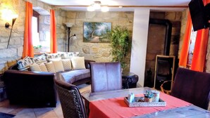 Ein gemütliches Wohnzimmer mit Steinwand, Kamin, einer Sofagarnitur und einem Esstisch mit rotem Tischläufer.