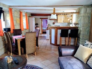 A cozy living room with a dining area, a kitchen with bar stools, and a stone wall.