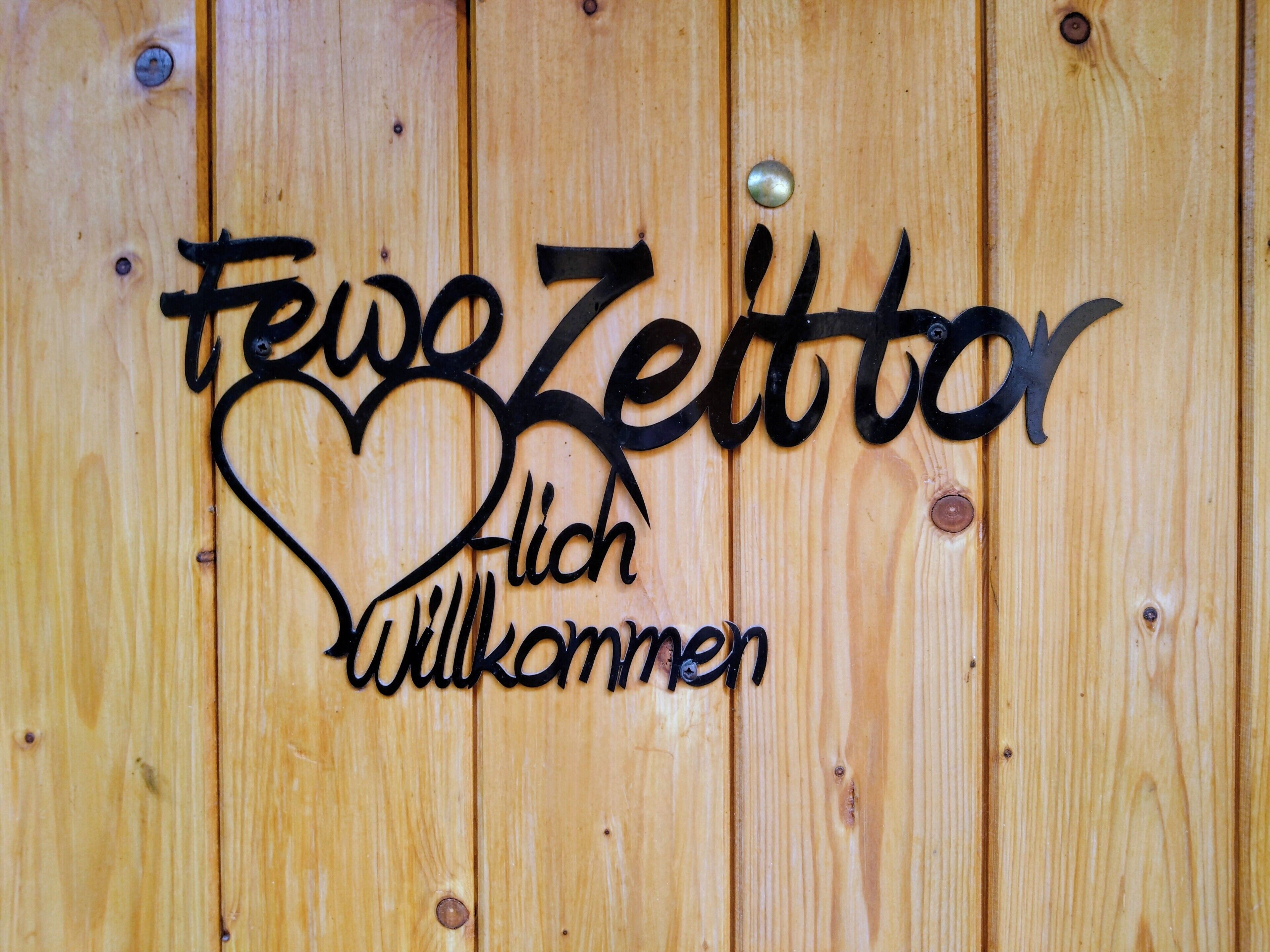 A wooden wall with a metal sign that reads 'Frei Zeit' and 'Willkommen' with a heart shape.