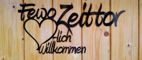 A wooden wall with a metal sign that reads 'Frei Zeit' and 'Willkommen' with a heart shape.