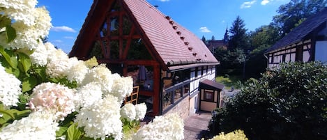 A traditional chalet with a steep red roof, surrounded by lush white flowers.