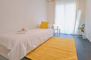 A bedroom with a bed, a bedside table, a lamp, a small table with a candle, a window with curtains, and a plant. - Luxury Corba Lake View Apartment with Terrace (Canobbio)
