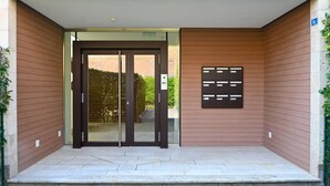 A building entrance with a double door, a small outdoor seating area, and a wall-mounted information board. - Luxury Corba Lake View Apartment with Terrace (Canobbio)