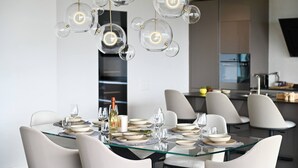 A modern dining area with a glass table set for a meal, surrounded by white chairs. - Luxury Corba Lake View Apartment with Terrace (Canobbio)