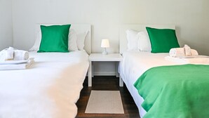 A hotel room with two beds, each with white bedding and green pillows, a nightstand with a lamp, and a small rug on the floor. - Luxury Corba Lake View Apartment with Terrace (Canobbio)