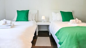 Ein Hotelzimmer mit zwei Betten, jeweils mit weißer Bettwäsche und grünen Kissen, einem Nachttisch mit Lampe sowie einem kleinen Teppich auf dem Boden.