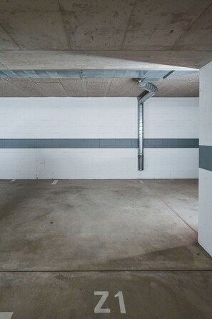 An empty parking garage with a concrete floor marked 'Z1' and a metal ventilation duct. - Luxury Corba Lake View Apartment with Terrace (Canobbio)